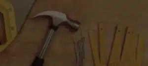This image shows a claw hammer a common tool used in masonry and construction work The hammer has a silver metal head and a wooden handle It is positioned on a wooden surface likely a workbench or shelf alongside some other tools such as rulers or measuring devices The background appears to be a warm wooden-toned interior suggesting this is a workshop or work area