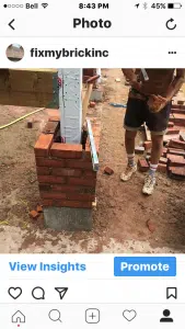 This image shows a close-up view of a masonry construction site The main focus is on a partially built brick wall with bricks and construction materials visible on the ground A persons legs and feet can be seen in the foreground wearing work boots and standing on the dirt ground The image provides a glimpse into the process of brick masonry work