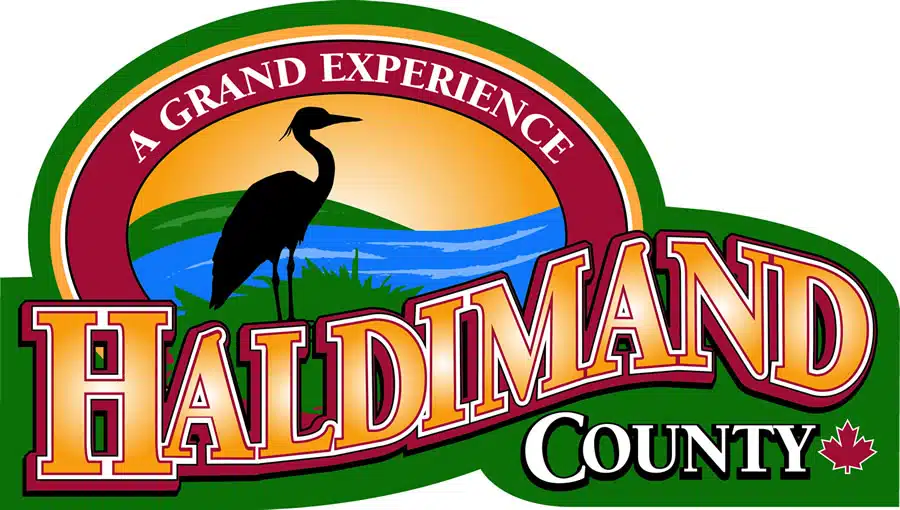 The image shows the logo for Haldimand County which appears to be a tourism or regional branding logo The logo features a silhouette of a heron or similar wading bird against a sunset landscape with water surrounded by a circular border that says A Grand Experience and Haldimand County in large text The logo has a colorful vibrant design that evokes the natural beauty and outdoor experiences associated with the Haldimand County region