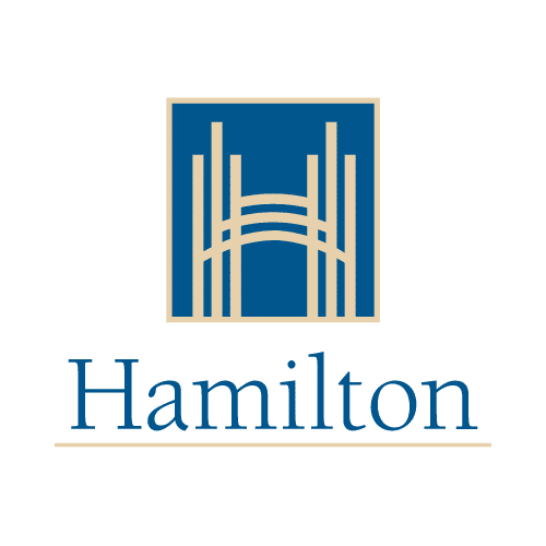 The image shows the logo for the city of Hamilton The logo consists of a square frame with a series of vertical lines or columns in the center creating a stylized architectural or skyline-like design The word Hamilton is displayed below the graphic element in a simple clean font The overall color scheme uses shades of blue and tan giving the logo a professional and modern aesthetic