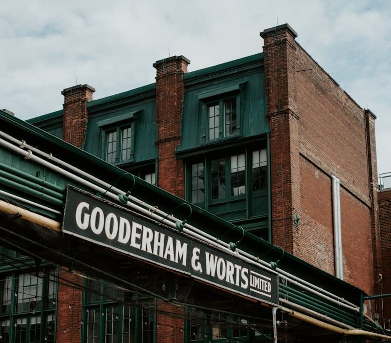 This image shows the exterior of a brick building with a prominent sign that reads GOODERHAM WORTS LIMITED The building has a green roof and several large windows The architecture features distinctive brick chimneys and a sturdy industrial-style design The image conveys a sense of history and the buildings connection to the Gooderham Worts company which was likely a prominent business or manufacturer in the area