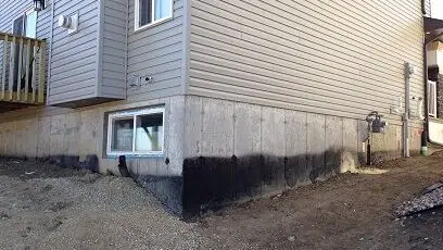 A home's exposed concrete foundation is visible, showing signs of wear and staining that could be concealed with a parging treatment.