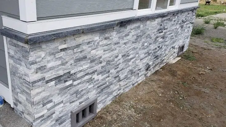 
The exterior of a home features a stone veneer siding along its foundation, providing a textured and stylish alternative to traditional parging. The varied gray shades of the stone complement the home's siding color and create visual interest